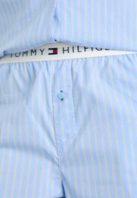 Ljusblå randiga boxer shorts med en vit elastisk midjeband med "TOMMY HILFIGER"-logotyp och en blå knapp fram.