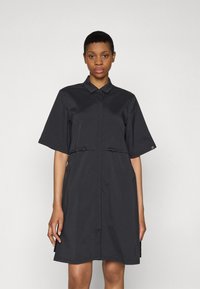 Abito nero in tessuto morbido, con colletto a camicia, maniche corte e vita cinchata con piccoli lacci sul davanti.