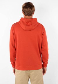 Sweatshirt à capuche couleur rouille avec une poche kangourou, des poignets et un ourlet côtelés. Présente un accent de logo sur l'épaule gauche.