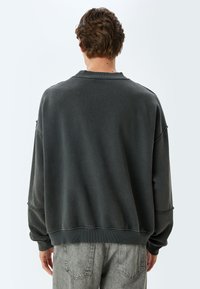 Donkergrijze sweatshirt met een ontspannen pasvorm, ribgebreide manchetten en zoom. Textuurstof, minimale stikdetails en een ronde halsontwerp.