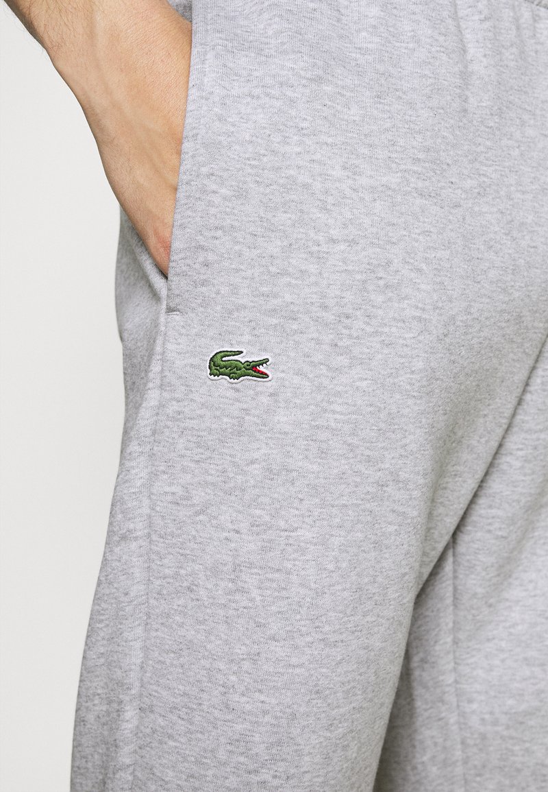 Szare dresy wykonane z mieszanki bawełnianej o gładkiej fakturze. Posiadają wyszywane zielone logo krokodyla po boku.