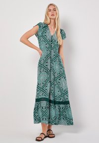 Langes, gemustertes grünes Kleid mit V-Ausschnitt, kurzen Puffärmeln und einem gestuften Saum mit Spitze. Leichter Stoff mit komplexem Design.