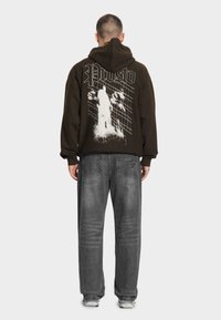 Czarna bluza z kapturem z białym wzorem graficznym na plecach, z napisem "Prosto" i grafiką. W zestawieniu z szarymi luźnymi dżinsami i trampkami.