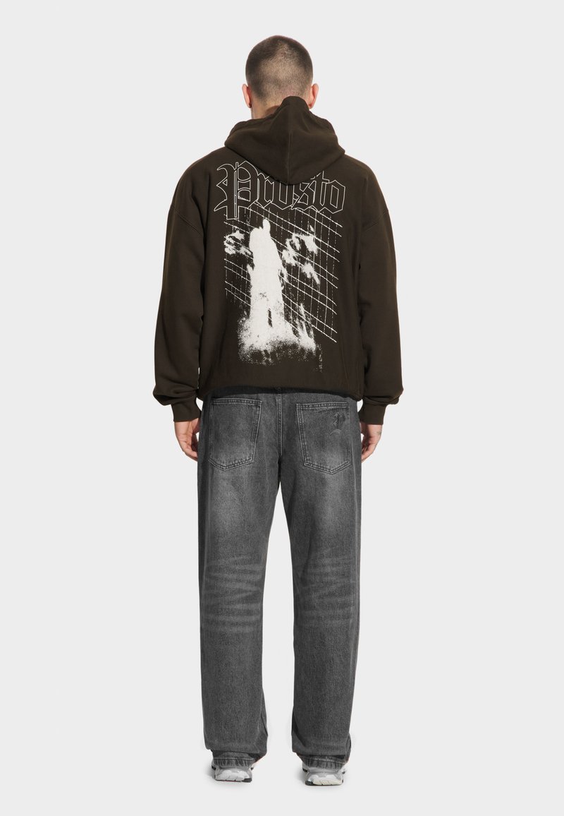 Czarna bluza z kapturem z białym wzorem graficznym na plecach, z napisem "Prosto" i grafiką. W zestawieniu z szarymi luźnymi dżinsami i trampkami.