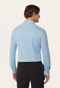 Lichtblauwe langemouwen shirt met een puntkraag, textuurstof, contrasterende knopen op de manchetten, gecombineerd met donkere broek.