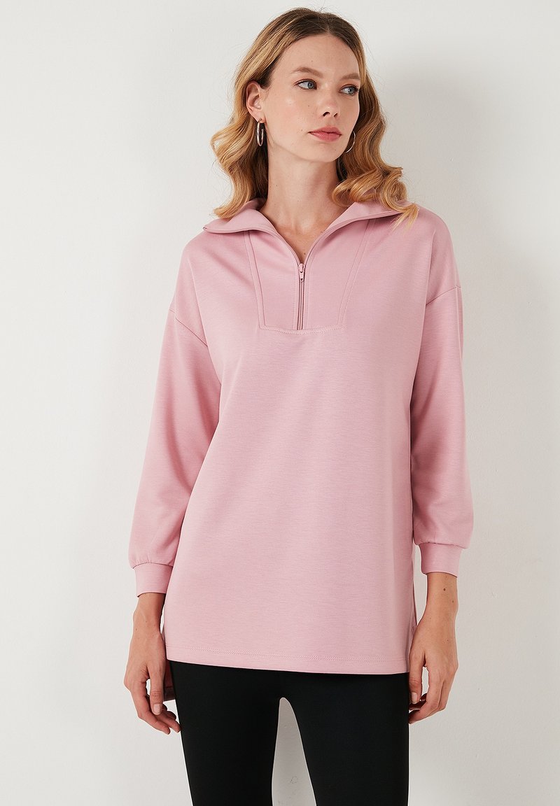 Felpa rosa con zip, colletto alto, maniche lunghe e vestibilità rilassata. Il tessuto sembra morbido con una texture liscia.