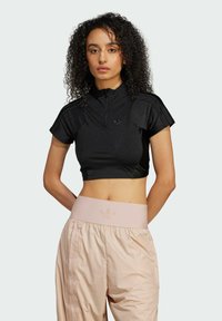 Black cropped athletic top with short sleeves, high collar, and front zipper; paired with light pink, high-waisted athletic pants.