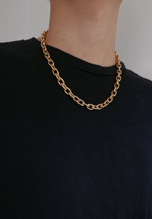 Goldene Kettenhalskette aus miteinander verbundenen ovalen Formen, die auf einem schwarzen T-Shirt liegt. Glatte Textur mit polierter Oberfläche.