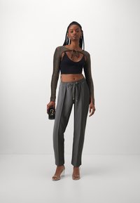 Top court noir avec de longues manches pailletées, associé à un pantalon gris à cordon de serrage. Des sandales à talons transparents et une pochette noire complètent le look.