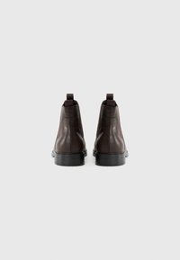 Botas de tobillo de cuero marrón con una textura suave, paneles laterales elásticos y una suela de goma negra. Incluyen tiradores para facilitar su uso.