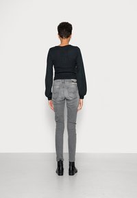 Černý přiléhavý svetr s dlouhými rukávy, kombinovaný se šedými skinny džíny. Modelka oblečená v černých kotníkových botách, viděná zezadu na jednobarevném pozadí.