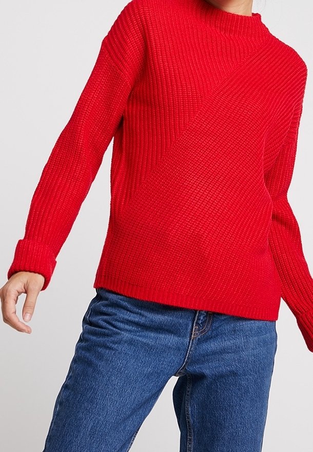Röd stickad tröja med ribbat mönster, med långa ärmar och hög krage. I kombination med blå jeans.