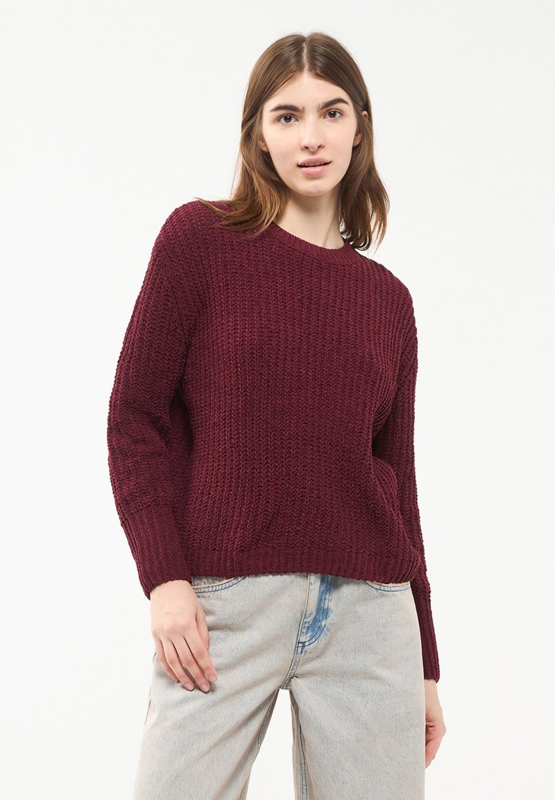 Maglione borgogna a maglia con scollo rotondo, maniche lunghe e motivo testurizzato. Abbinato a jeans in denim azzurri.