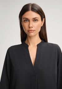 Zwarte, lichte blouse met een V-hals en een subtiele kraag. Voorzien van lange mouwen en een gladde textuur. Geen zichtbare patronen of versieringen.