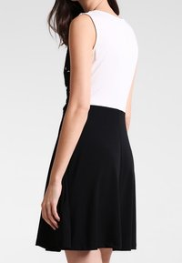 Robe sans manches noir et blanc avec un corsage ajusté et une jupe évasée. Tissu lisse avec des couleurs contrastées et des lignes simples.