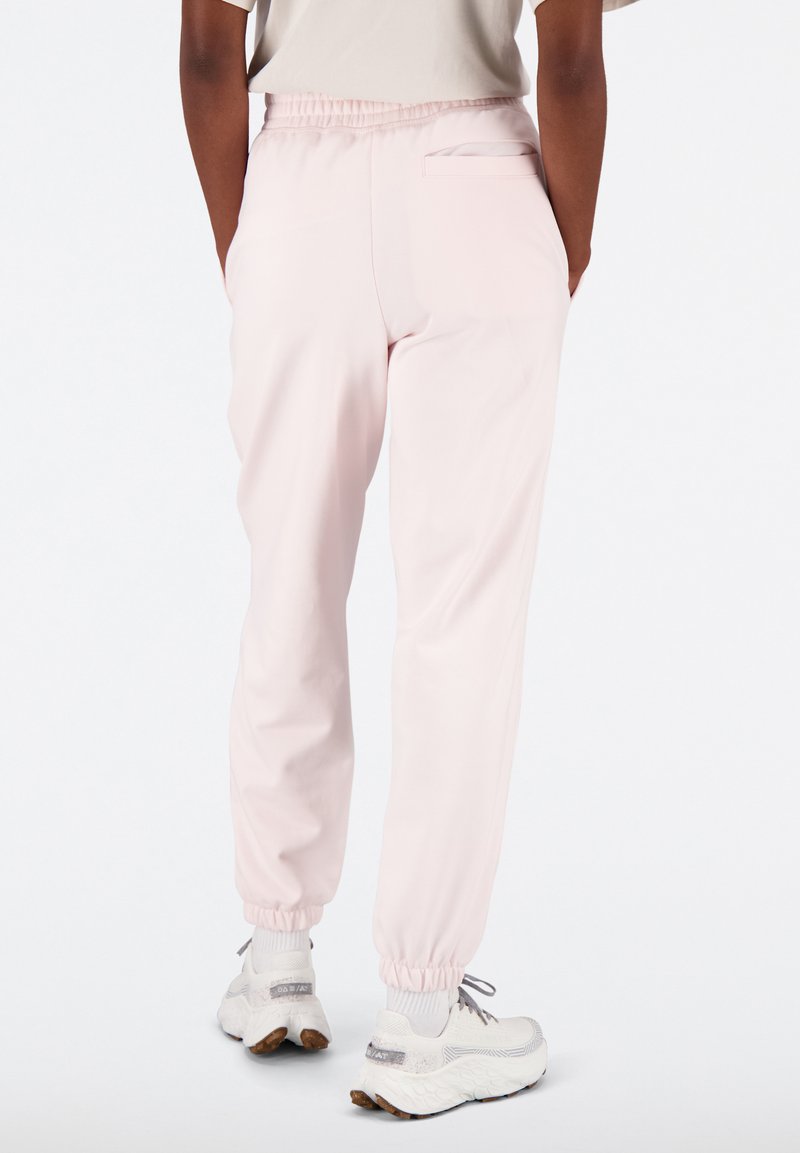 Joggers rose clair avec une taille élastique, une poche latérale et des chevilles resserrées, fabriqués en tissu lisse et léger.
