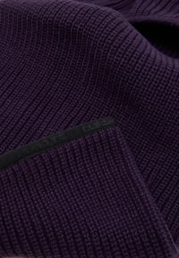 Lilla ribbet strikket hue med en tekstureret stof. Har et sort bånd med præget tekst, hvilket giver et tæt og moderne look.