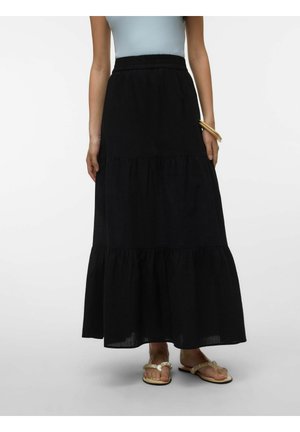 Kvinde iført sort lagdelt maxinederdel, lyseblå ærmeløs top, beige flettede sandaler og træ armbånd på håndleddet.