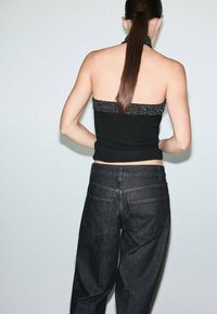 Top negro tipo halter con un escote texturizado brillante, combinado con jeans de mezclilla oscuros de tiro alto que presentan un diseño clásico de bolsillos.