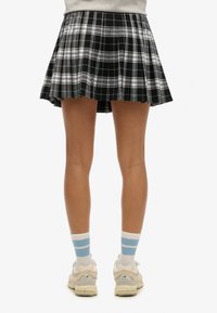 Zwart-wit geblokte plissé rok met een korte silhouette. Draagt met lichtblauwe gestreepte sokken en neutrale sportschoenen.