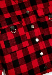 Rød og sort ternet flanneljakke med sølvknapper, brystlommer og et faux læder detaljer med en metalring.