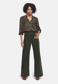 Chemise noire avec un motif abstrait léger, associée à un pantalon large olive. La tenue présente une coupe décontractée et un tissu doux.