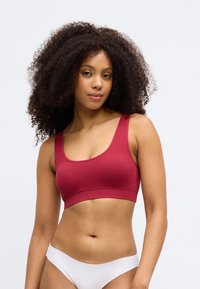 Červený rebrovaný bralet s širokými ramienkami a elastickým pásom; model je skombinovaný s bielym hipster spodným prádlom, ktoré predvádza hladkú textúru.