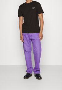 T-shirt en coton noir avec le logo "TOMMY JEANS", associé à un jean en denim violet clair et des chaussures en cuir noires. Tenue décontractée au design simple.