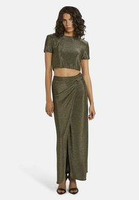 Zwei-Teile-Outfit, bestehend aus einem cropped Top und einem high-waisted Rock aus metallisch olivgrünem Stoff, mit einem Knoten-Detail und einem seitlichen Schlitz.