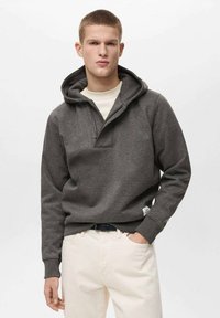 Felpa con cappuccio grigio scuro, con zip frontale a metà, tasca a marsupio e polsini a costine, abbinata a pantaloni color crema.
