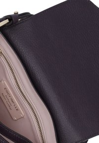 Borsa a tracolla in pelle viola con chiusura a zip, dotata di una soffice fodera interna rosa e di un'etichetta del marchio. Superficie testurizzata e dettagli in hardware dorato.