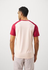 Kortermet treningsskjorte med lys rosa kropp og mørkerøde ermer. Glatt tekstur, rund halsdesign og sidekantdetaljer.