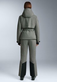 Šedá vzorovaná bunda s kapucňou a opaskom v páse, kombinovaná s rozšírenými nohavicami s čiernymi panelovými akcentmi. Hladká textúra, strih na mieru.