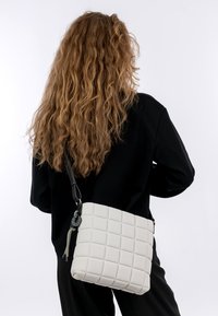 Borsa a tracolla leggera di un grigio chiaro con motivo a quadri, realizzata in materiale morbido, con una tracolla nera regolabile e hardware decorativo.
