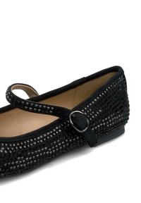 Zapato plano negro con parte superior de tejido texturizado, con punta redondeada y una tira de estilo Mary Jane con un hebilla metálica. Forro interior suave.