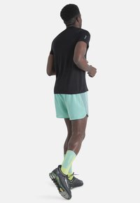 Camiseta atlética negra, pantalones cortos verde menta con acentos reflectantes, calcetines atléticos amarillos brillantes y zapatillas de correr negras con detalles verdes.