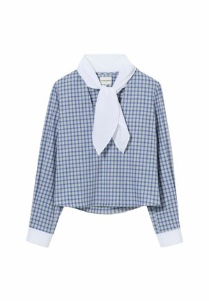 Femme portant une chemise bleue à carreaux avec une écharpe blanche, un pantalon beige à jambes larges, des chaussures noires, une ceinture marron, tenant un petit sac à main marron.