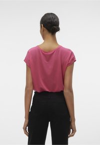 T-shirt a maniche corte, morbido e leggero, in cotone rosa brillante, con scollo ampio e maniche arrotolate, abbinato a jeans neri a vita alta.