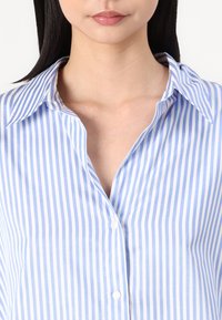 Blue and white striped button-up shirt with a collar, featuring a smooth texture and vertical stripes of varying widths.