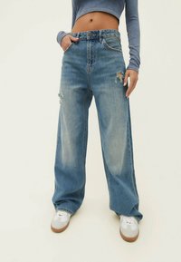 Ljusblå vida jeans med hög midja och slitdetaljer. Bärs med en figurnära långärmad topp och vita sneakers.