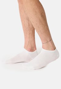 Hvide ankelsokker med en glat tekstur, en ribbet manchet og små ventilationshuller langs siderne, båret på bare fødder.