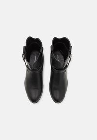 Botines de cuero negro con una textura suave, cuello con ondas y detalle de hebilla lateral. El interior presenta un forro negro.