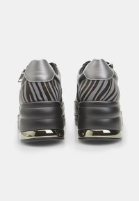 Sneakers neri e argento con design a strisce zebra, presentano un tallone imbottito, suola chunky e dettagli metallici. Dettaglio con cerniera sul retro.