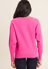 Felroze trui met een losse pasvorm, geribbelde manchetten en tailleband. Ronde halslijn, zachte textuur en afhangende schouders verhogen het comfort.