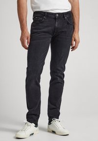 Svarta denimjeans med slim fit, som har fem fickor och en klassisk midja. Kombinerade med vita och gröna sneakers.
