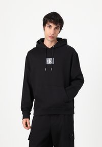 Czarna bluza z kapturem z mieszanki bawełny z przednią kieszenią, z kwadratową naszywką logo w białym i niebieskim kolorze. Ribbowe mankiety i dół.