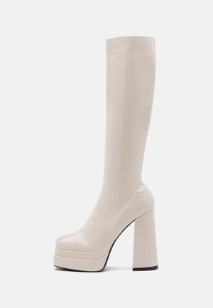 Wysoki beżowy platformowy but z lakierowanej skóry, z zaokrąglonym noskiem i grubym wysokim obcasem typu słupek.
