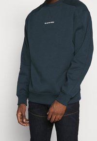 Sweat-shirt bleu foncé avec col rond, logo G-Star RAW sur la poitrine, poignets et ourlet côtelés, fabriqué en coton mélangé doux et texturé.