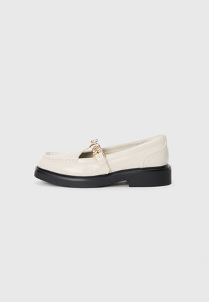 Hvite skinnloafers med rund tå, en liten svart gummisåle og detalj med gullspenne. Glatt tekstur med sømmer.