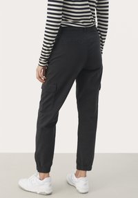Svarta cargo-byxor med elastiska ankle cuffs, sidofickor och en slät bomullstyg, kombinerat med en randig långärmad skjorta och vita sneakers.